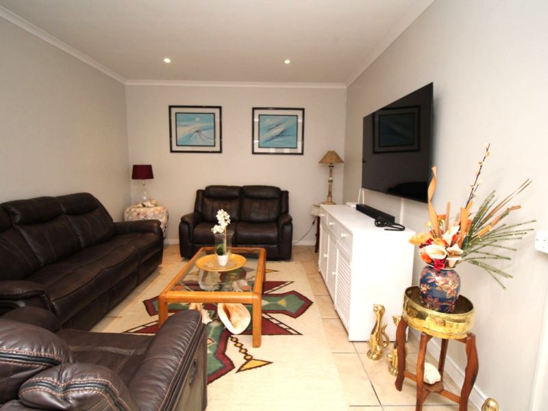 A comfortable living room featuring tiled flooring, recessed downlighting, and coved ceiling details, providing a functional and well-maintained space.