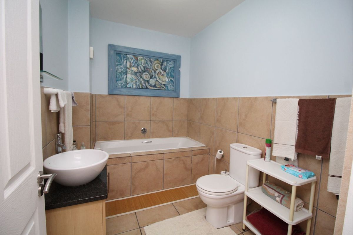 A functional bathroom featuring a built-in bathtub, tiled walls, a vanity with a vessel sink, and a standard toilet.