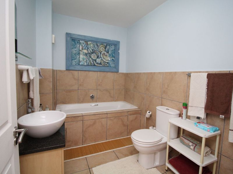 A functional bathroom featuring a built-in bathtub, tiled walls, a vanity with a vessel sink, and a standard toilet.