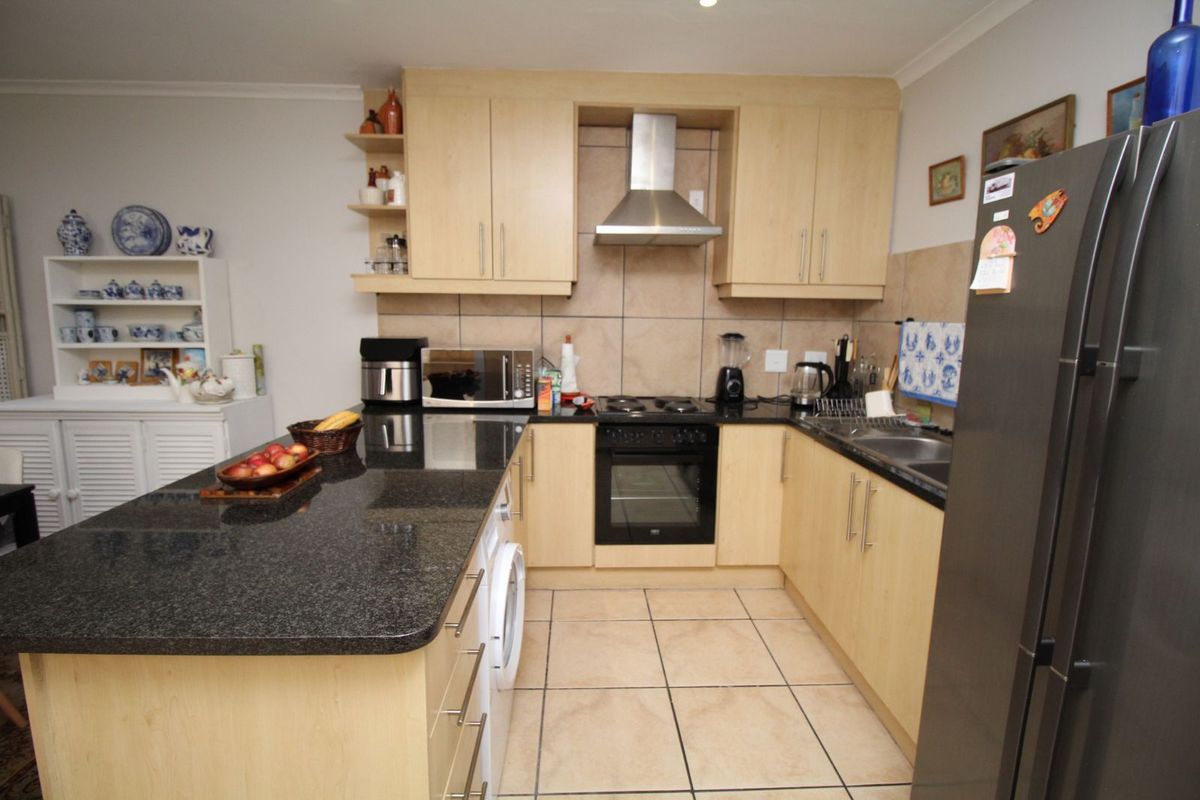 Functional kitchen featuring light wood cabinetry, granite countertops, tiled splashbacks, and integrated appliances including an oven and extractor fan.
