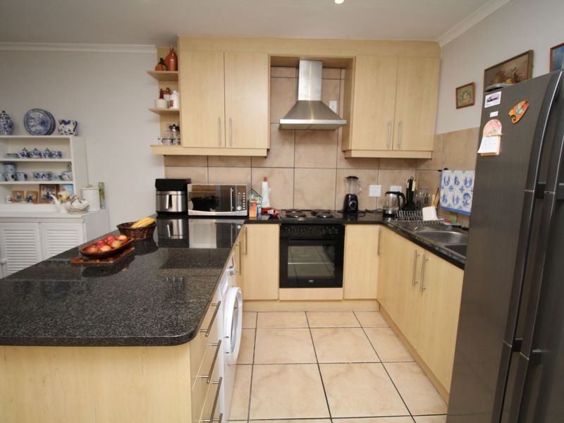 Functional kitchen featuring light wood cabinetry, granite countertops, tiled splashbacks, and integrated appliances including an oven and extractor fan.