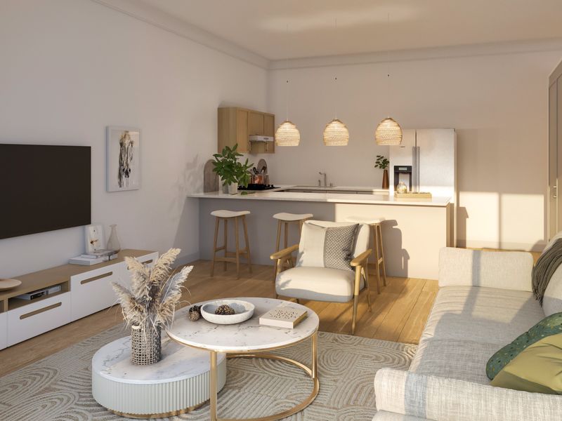 A bright open-plan living and kitchen area featuring modern cabinetry, a central island, and warm hardwood flooring, creating a cohesive and inviting living space.