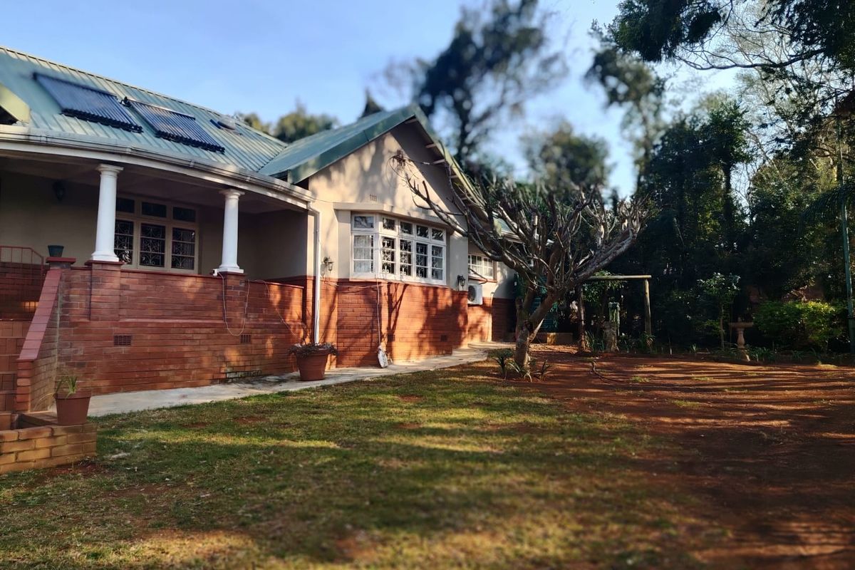 Rear view of a house featuring a brick facade, covered veranda with columns, and roof-mounted solar water heating panels set in a garden.