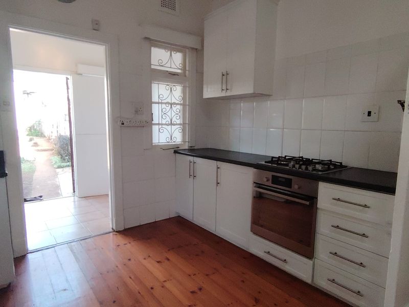 A functional kitchen featuring white cabinetry, a gas hob, built-in oven, tiled backsplash, and polished timber flooring with direct access to the exterior.