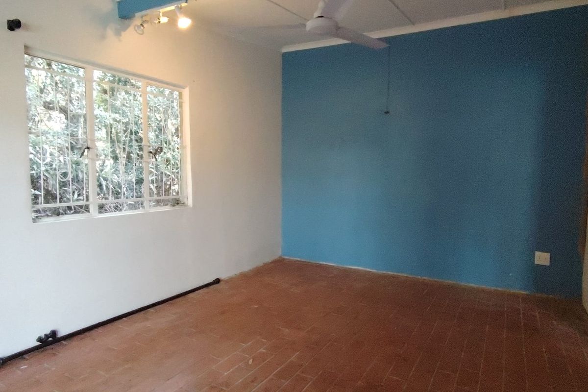 An empty bedroom featuring terracotta tile flooring, a ceiling fan, and a blue accent wall with security bars on the window.