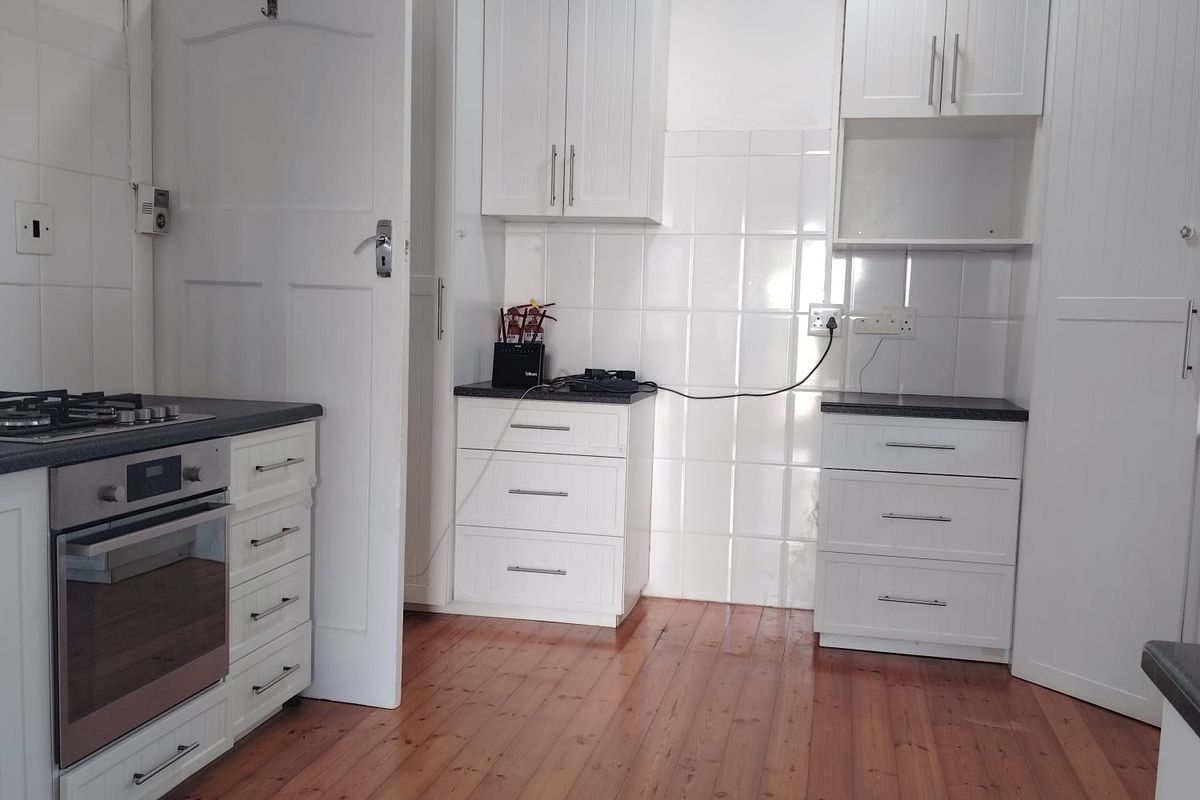 A clean, functional kitchen featuring white cabinetry, built-in oven and gas hob, tiled splashbacks, and warm timber flooring.