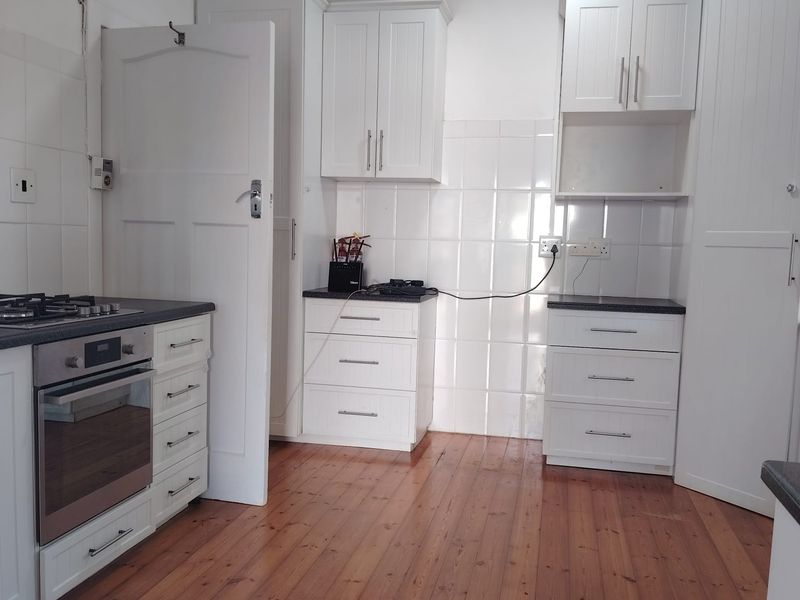 A clean, functional kitchen featuring white cabinetry, built-in oven and gas hob, tiled splashbacks, and warm timber flooring.