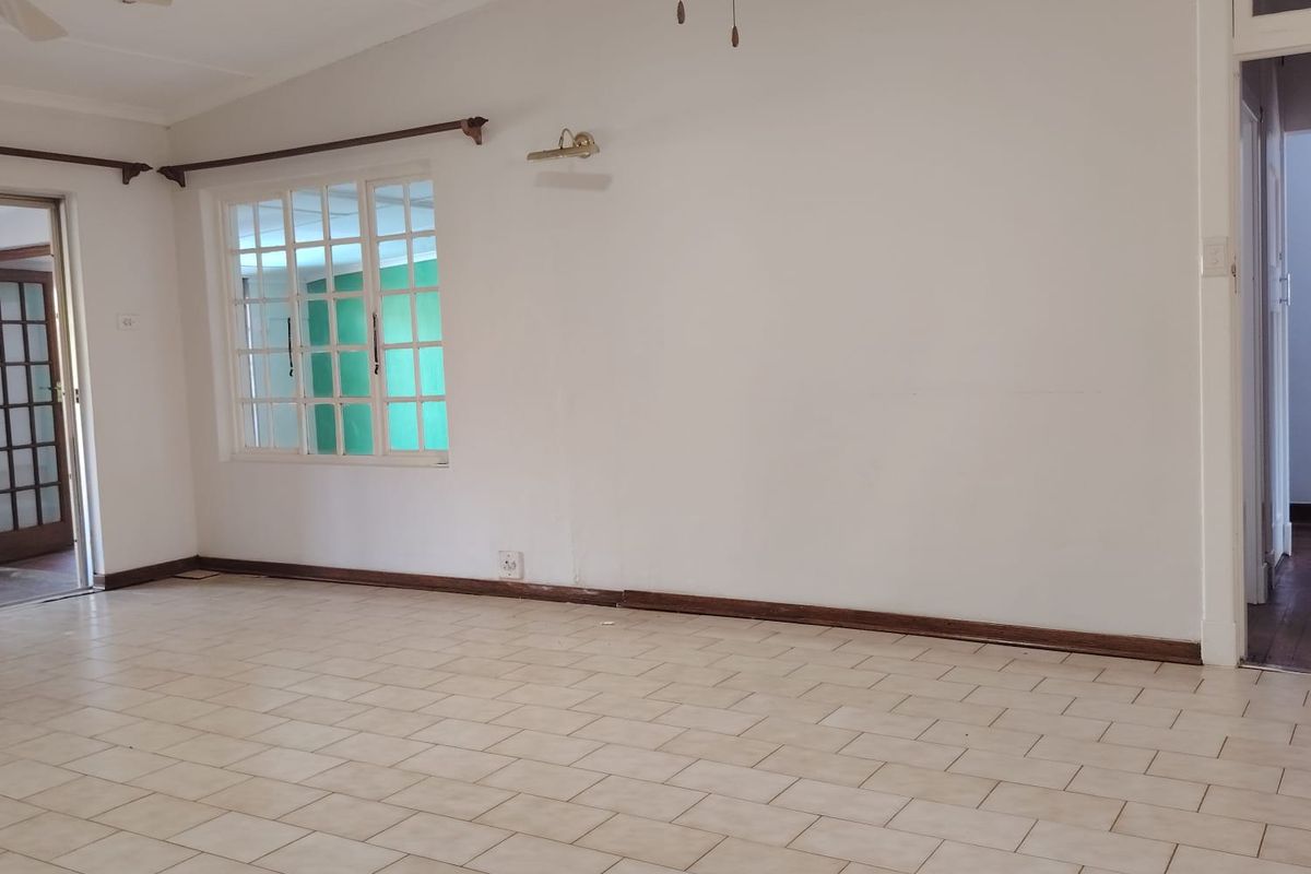 A spacious, empty living area featuring neutral tiled flooring, timber window frames, and a ceiling fan, offering a blank canvas for interior design.