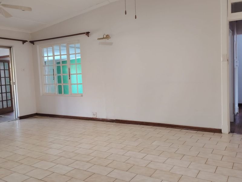 A spacious, empty living area featuring neutral tiled flooring, timber window frames, and a ceiling fan, offering a blank canvas for interior design.