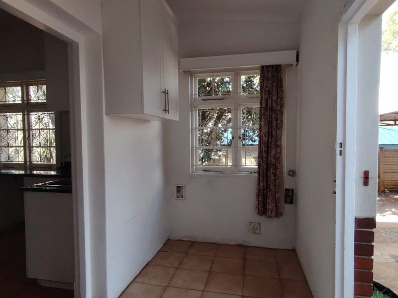 A functional, empty scullery or utility area featuring tiled flooring, wall-mounted cabinetry, and a window with security bars.