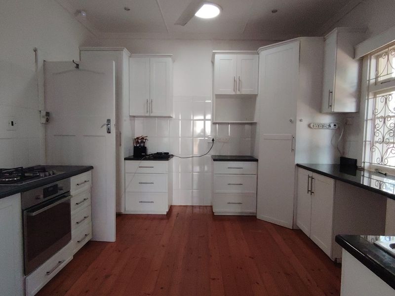 A functional kitchen featuring white cabinetry, dark countertops, gas hob, electric oven, and polished hardwood flooring with a ceiling fan.