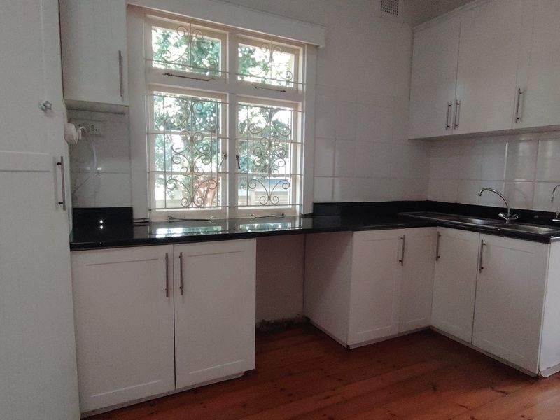A clean, empty kitchen featuring white cabinetry, black granite countertops, a stainless steel sink, and polished timber flooring.