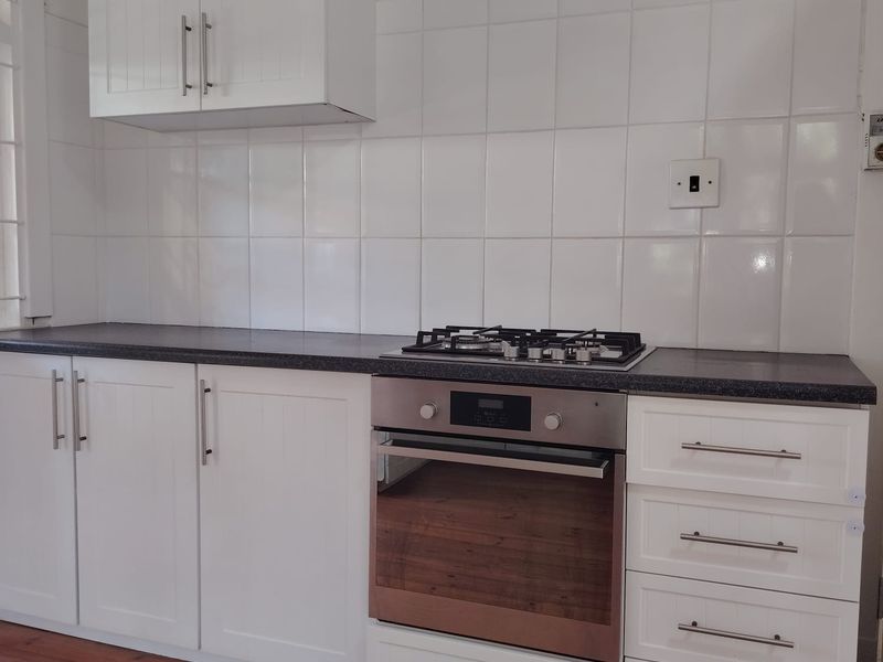 A clean, modern kitchen featuring white shaker-style cabinetry, dark laminate countertops, a gas hob, and a built-in oven with timber flooring.