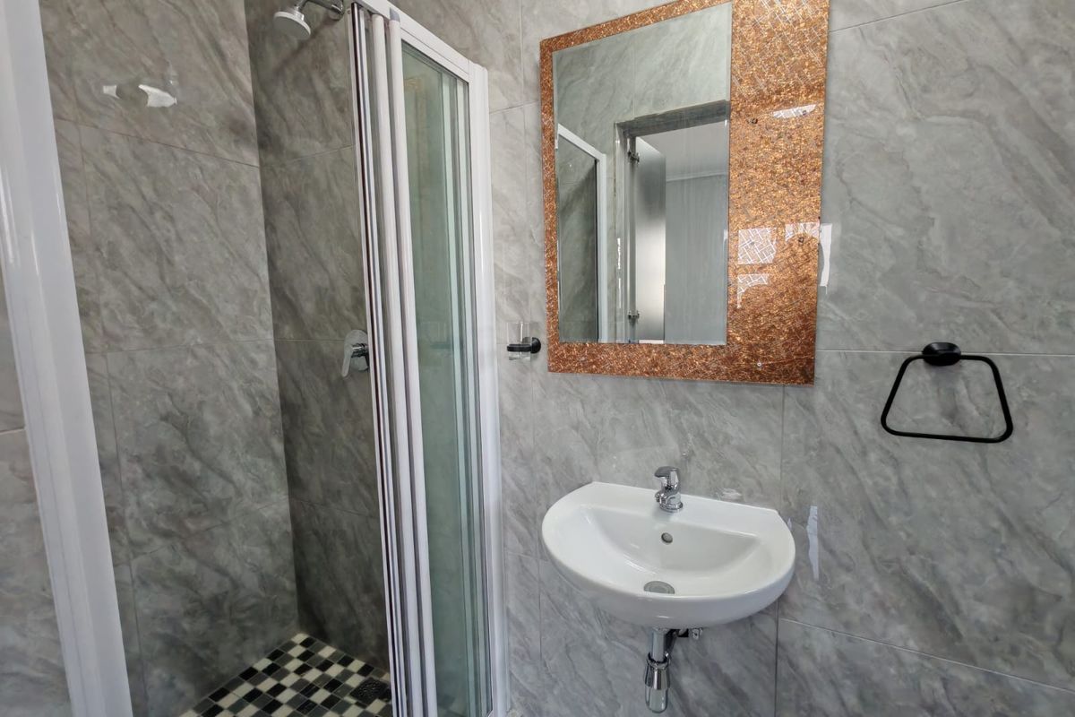 A modern bathroom featuring a shower enclosure with a checkered floor, a wall-mounted basin, and decorative tiled walls.