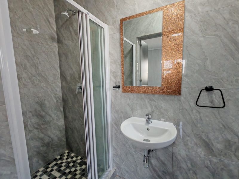 A modern bathroom featuring a shower enclosure with a checkered floor, a wall-mounted basin, and decorative tiled walls.
