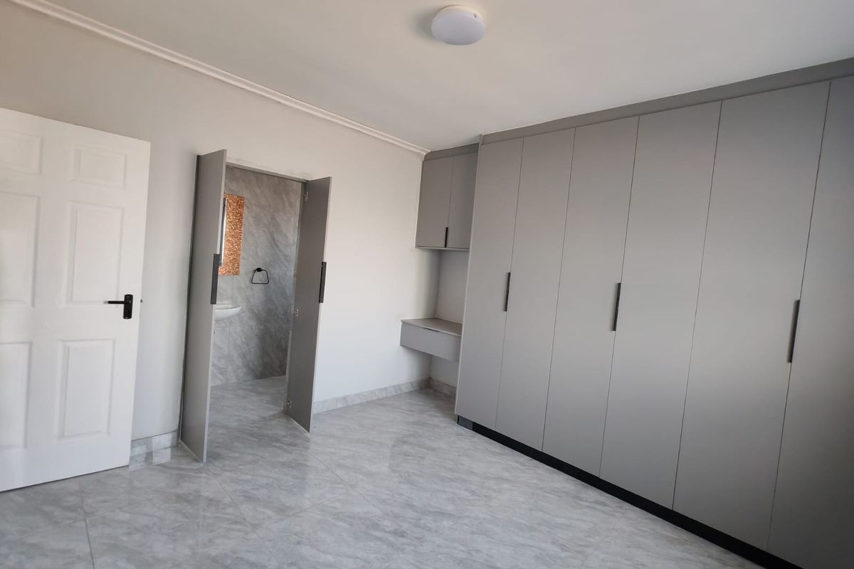 A bright, modern bedroom featuring neutral tiled flooring, extensive built-in grey cabinetry, and direct access to an en-suite bathroom.
