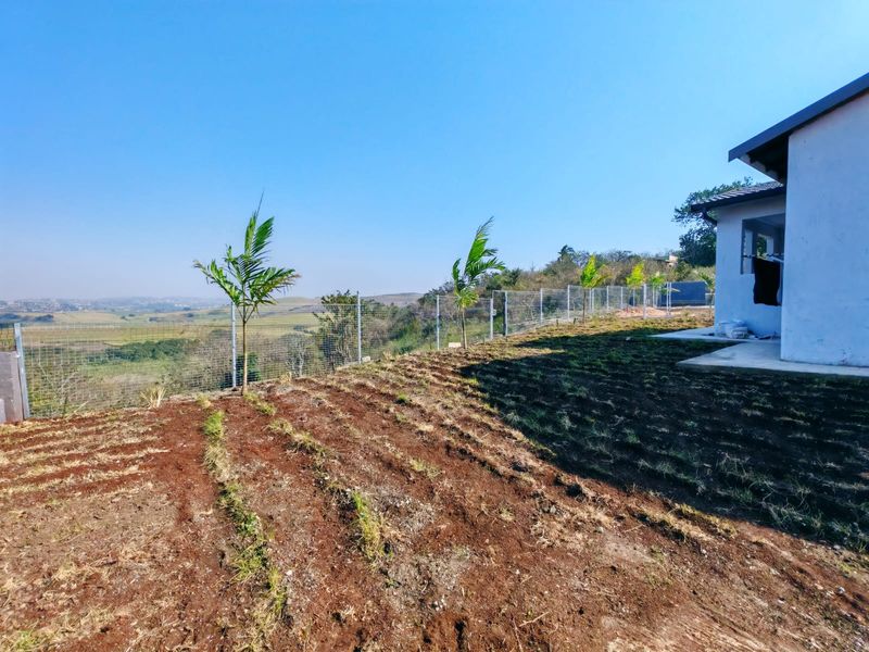 Rear exterior view of the townhouse featuring a concrete patio, wire mesh perimeter fencing, and an undeveloped garden area with scenic landscape views.