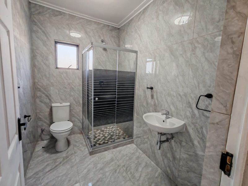 Modern bathroom featuring full-height marble-look wall tiles, a glass shower enclosure, a wall-mounted basin, and a standard toilet.