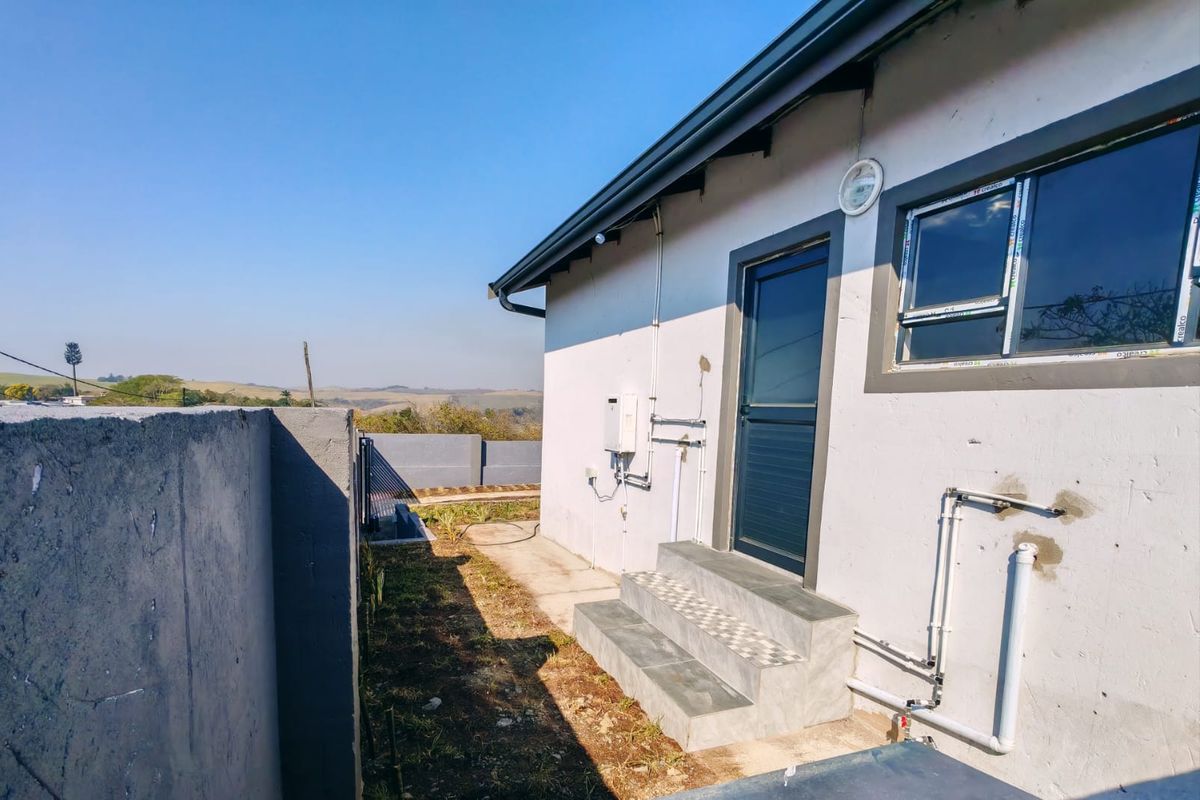 Rear exterior view of the townhouse featuring a gas geyser, tiled steps, and exposed external plumbing against a boundary wall.