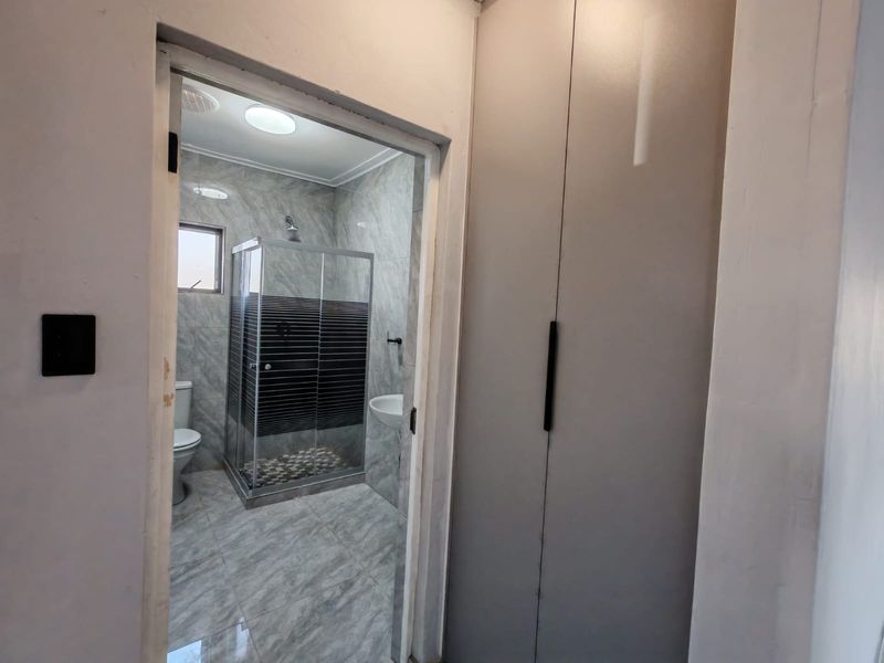 A modern bathroom featuring a glass shower enclosure, tiled walls and flooring, a toilet, a washbasin, and a tall built-in storage cupboard.