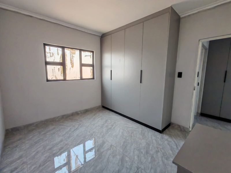 A clean, empty bedroom featuring modern grey built-in cupboards, neutral tiled flooring, and an aluminium-framed window.