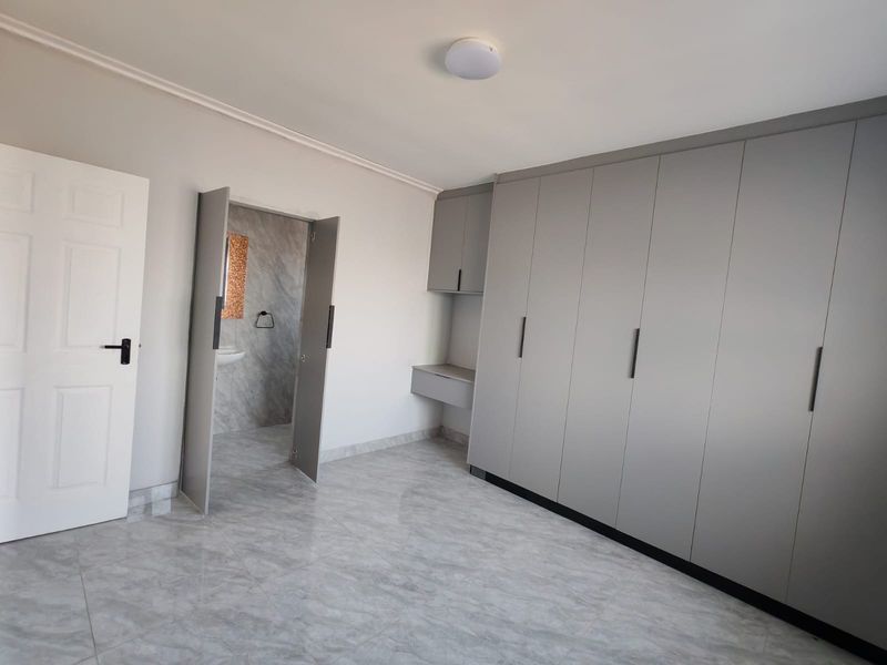 A clean, modern bedroom featuring neutral grey built-in cupboards, tiled flooring, and direct access to an en-suite bathroom.