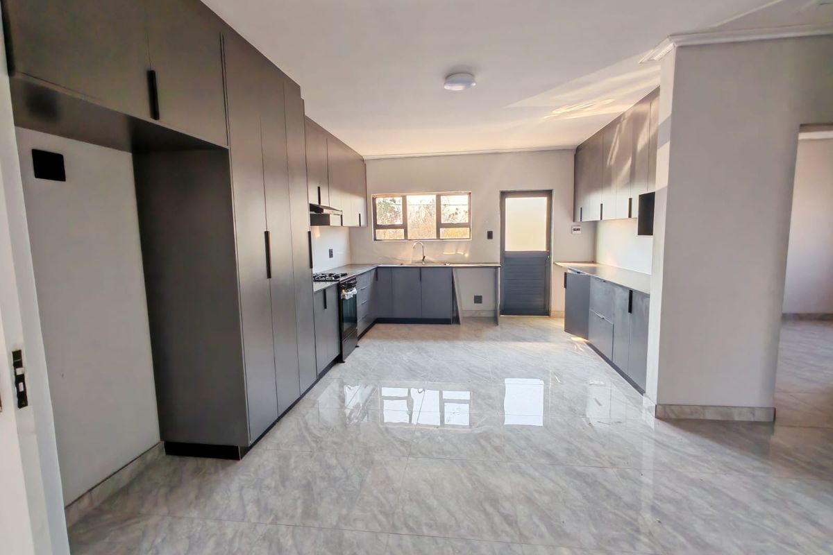 Modern kitchen featuring sleek grey built-in cabinetry, gas hob, oven, extractor fan, and polished tiled flooring with ample counter space.