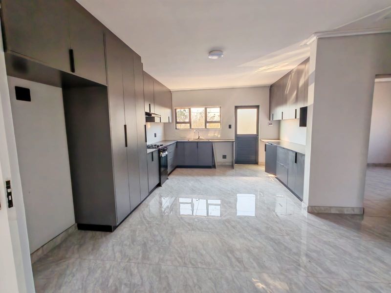 Modern kitchen featuring sleek grey built-in cabinetry, gas hob, oven, extractor fan, and polished tiled flooring with ample counter space.