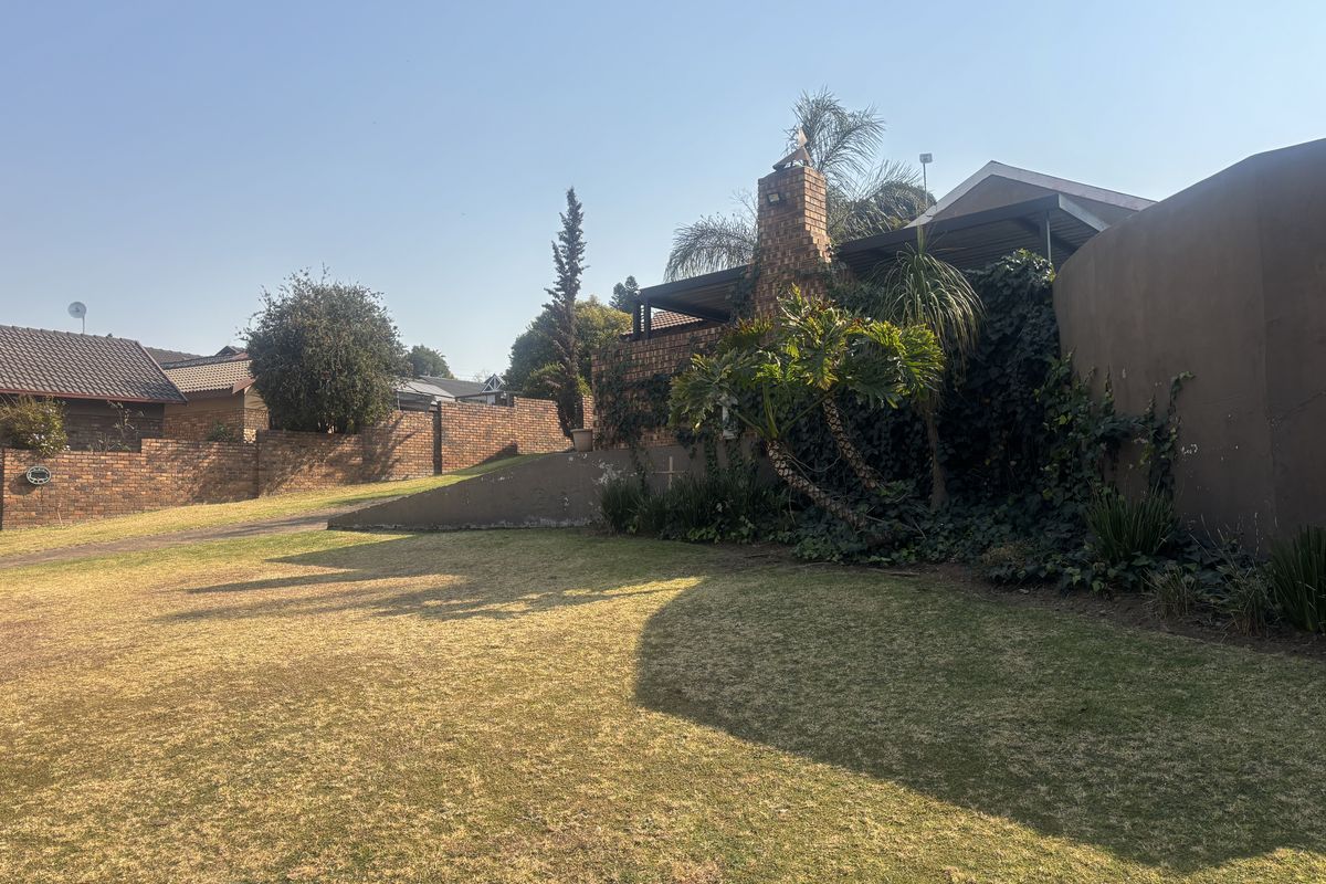 A view of the rear garden featuring a brick chimney, covered patio area, and established boundary walls.