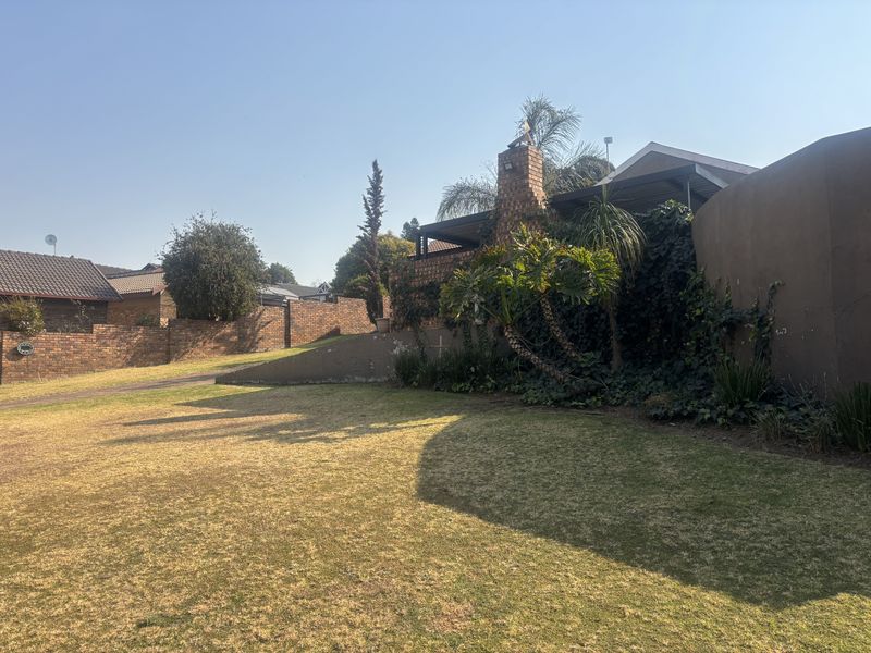 A view of the rear garden featuring a brick chimney, covered patio area, and established boundary walls.