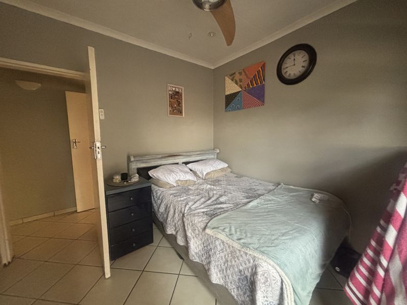A standard bedroom featuring neutral wall tones, tiled flooring, and a ceiling fan, providing a functional and comfortable sleeping space.