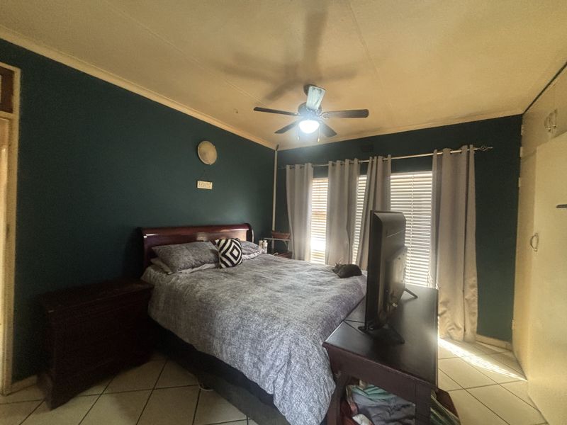 A bedroom featuring dark painted walls, tiled flooring, a ceiling fan, and built-in cupboard storage.