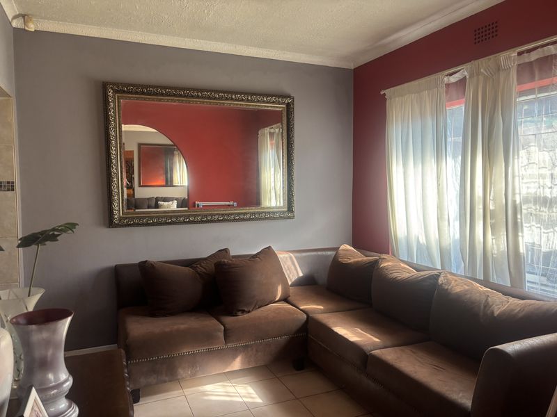A living room featuring tiled flooring, cornicing, and a dual-tone wall finish with natural light entering through the window.