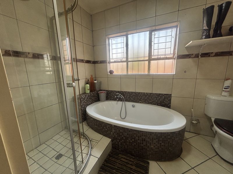 A functional bathroom featuring a glass shower enclosure, a built-in oval bathtub with mosaic tile detailing, and standard ceramic wall and floor tiling.