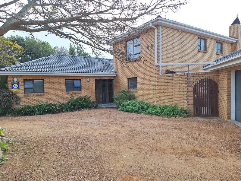 Front elevation of a double-storey face brick house featuring a tiled roof, gravel driveway, and secure gated entrance.