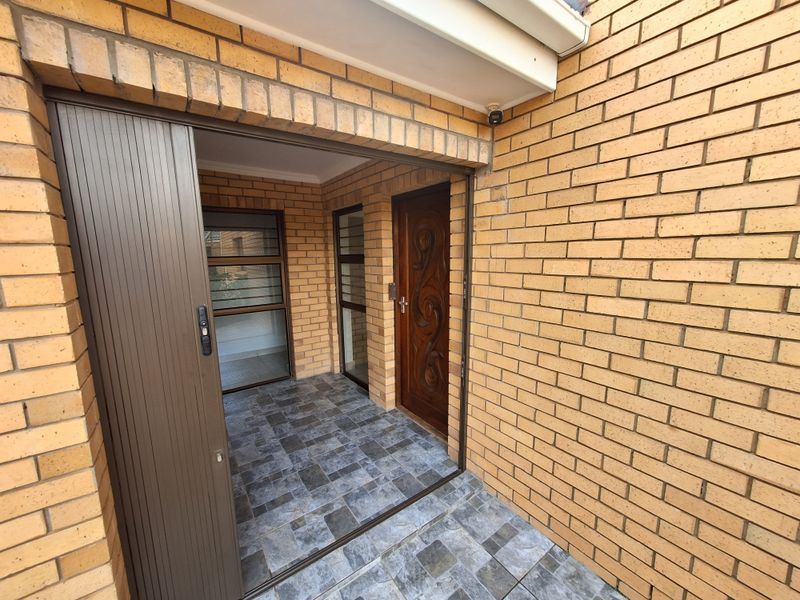 A covered entrance area featuring face brick walls, tiled flooring, and a solid wood front door with an integrated security gate.