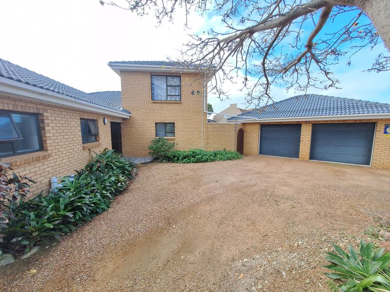 Front view of a face brick house featuring a double garage, tiled roof, and a gravel driveway with established garden beds.