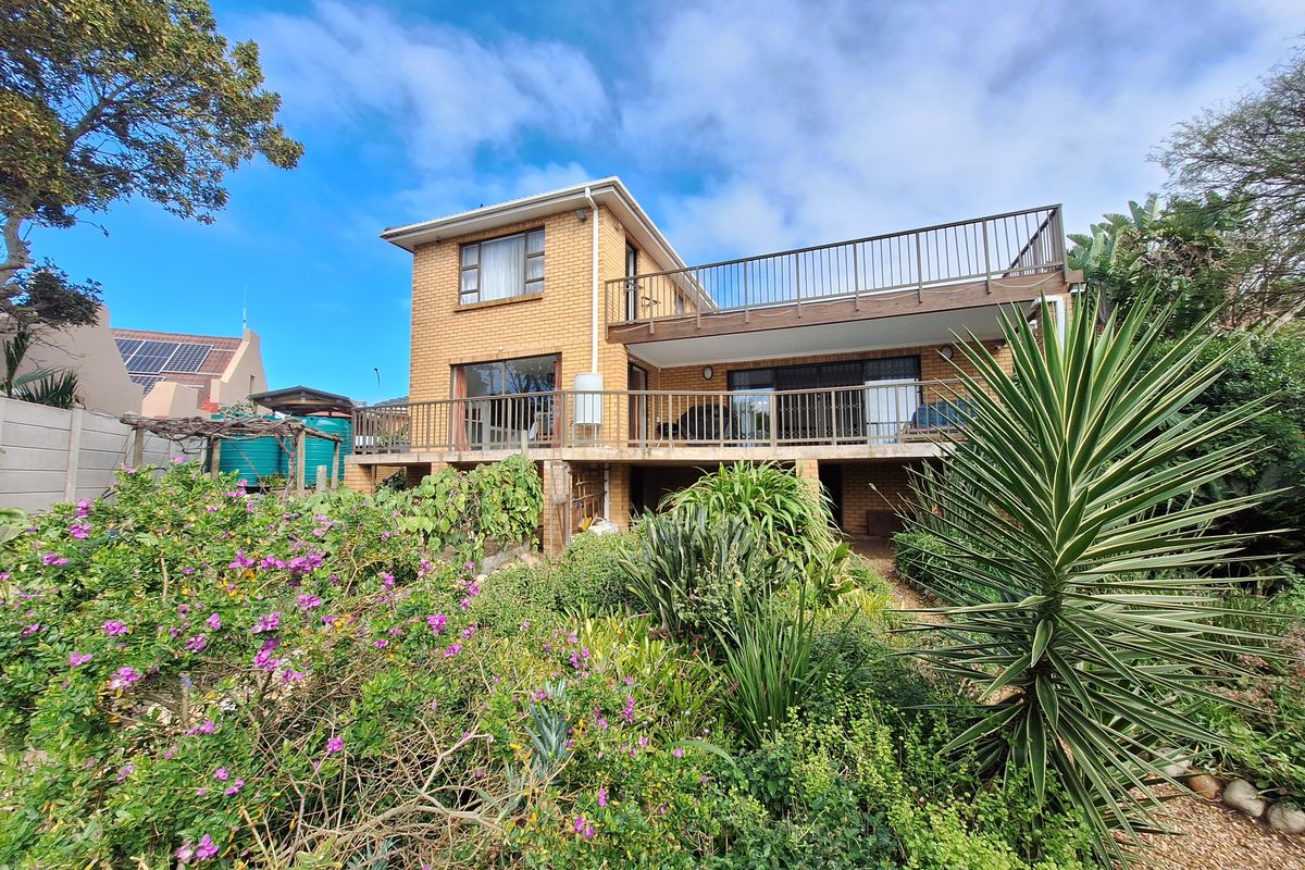 Rear view of a two-story brick house featuring a spacious balcony, sliding glass doors, and a well-established garden.