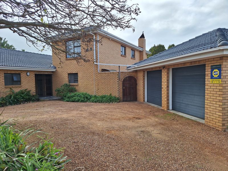 Front view of a face brick house featuring a double garage, gravel driveway, and secure gated entrance.