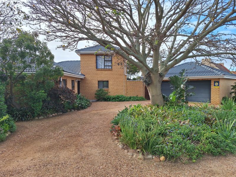 Front elevation of a double-story brick house featuring a gravel driveway, established garden, and a double garage.
