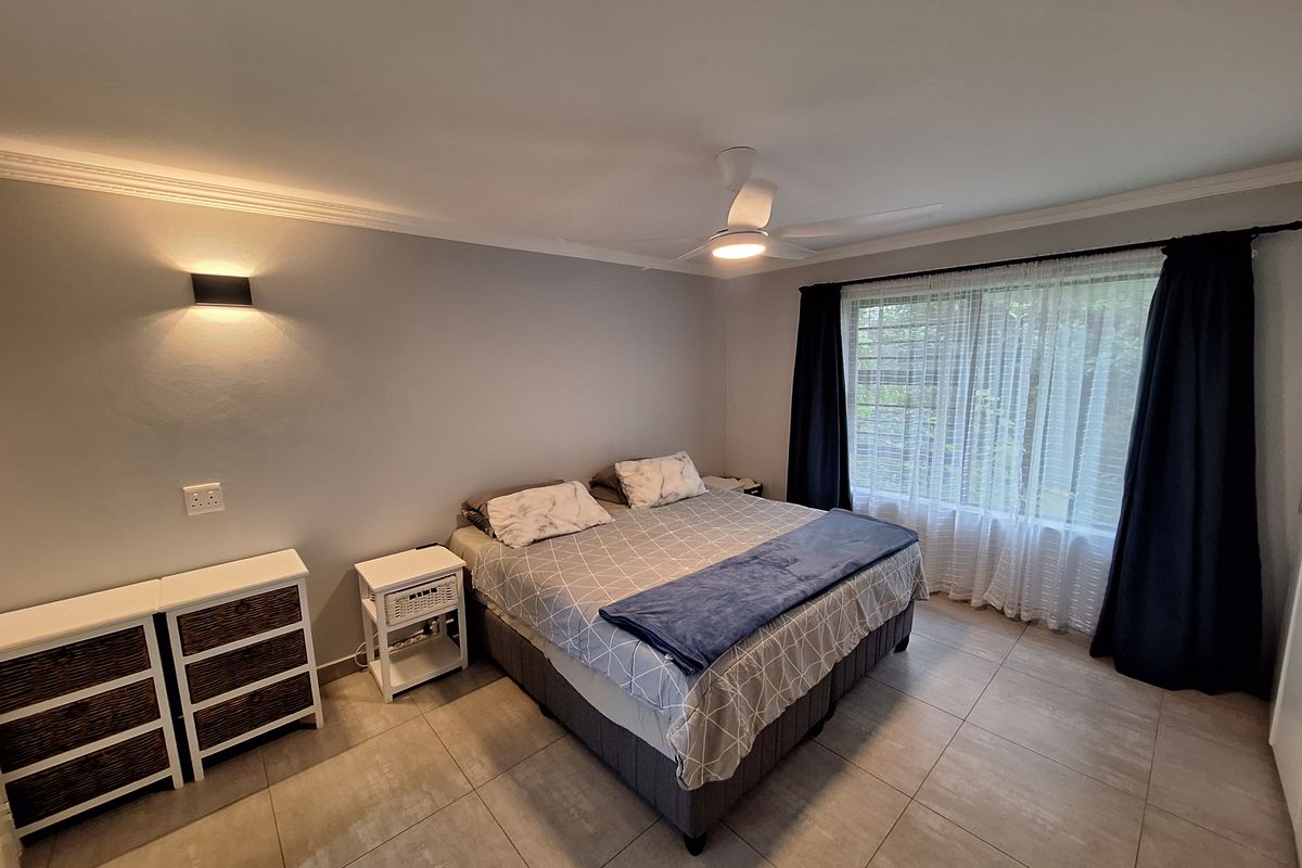 A well-maintained bedroom featuring neutral tiled flooring, a modern ceiling fan, and wall-mounted lighting, creating a comfortable and functional living space.