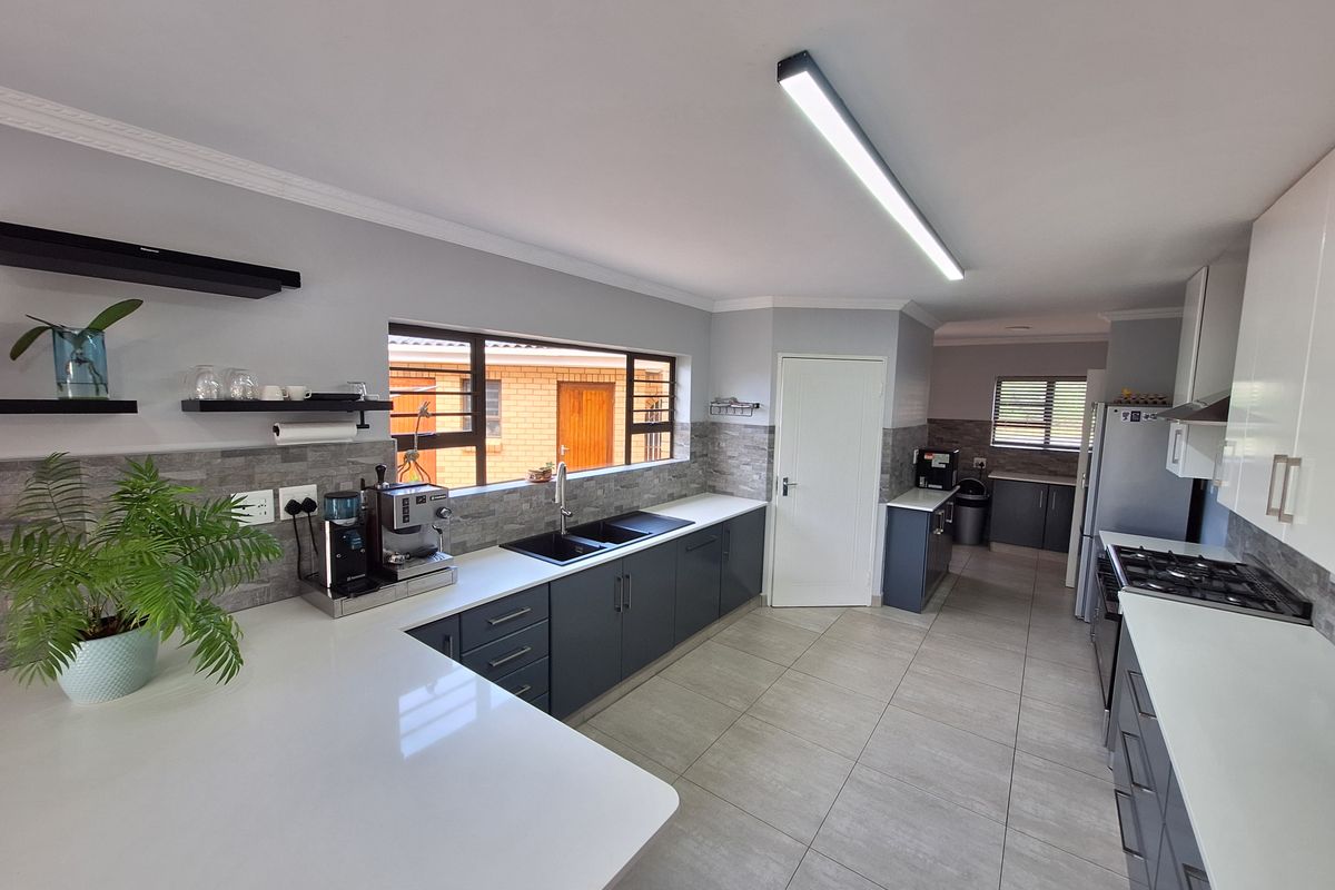 Modern kitchen featuring dark grey cabinetry, white quartz countertops, a gas hob, and tiled flooring with ample natural light.