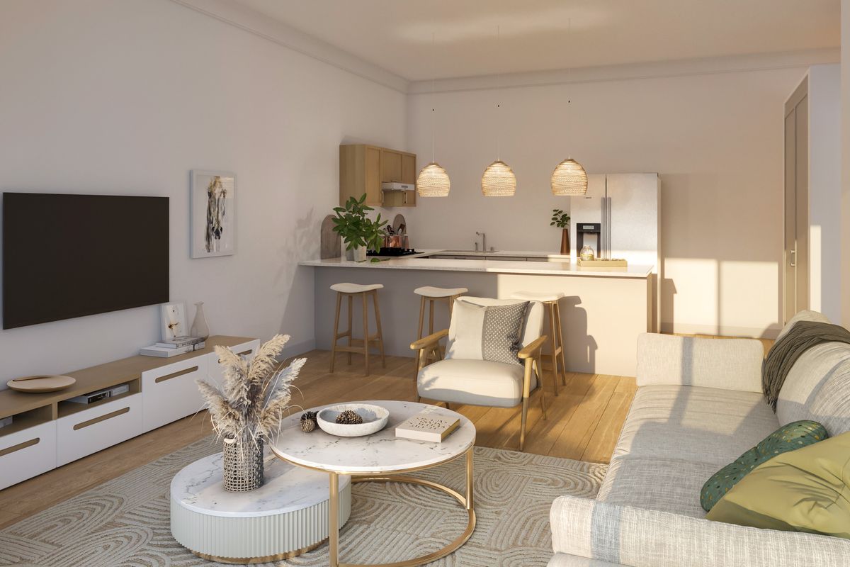A bright open-plan living and kitchen area featuring modern cabinetry, a central island, and warm hardwood flooring, creating a cohesive and inviting living space.