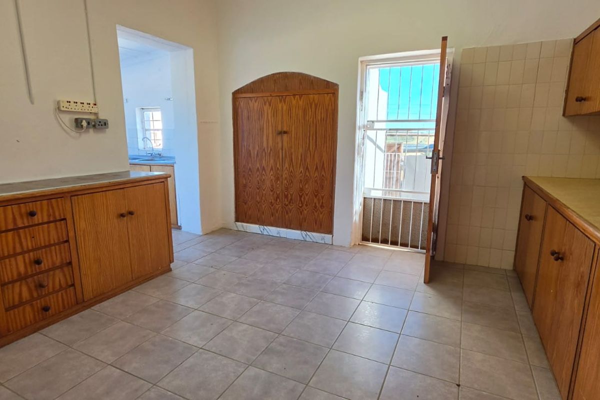 A functional kitchen space featuring extensive built-in wooden cabinetry, tiled flooring, and direct access to the exterior via a security gate.