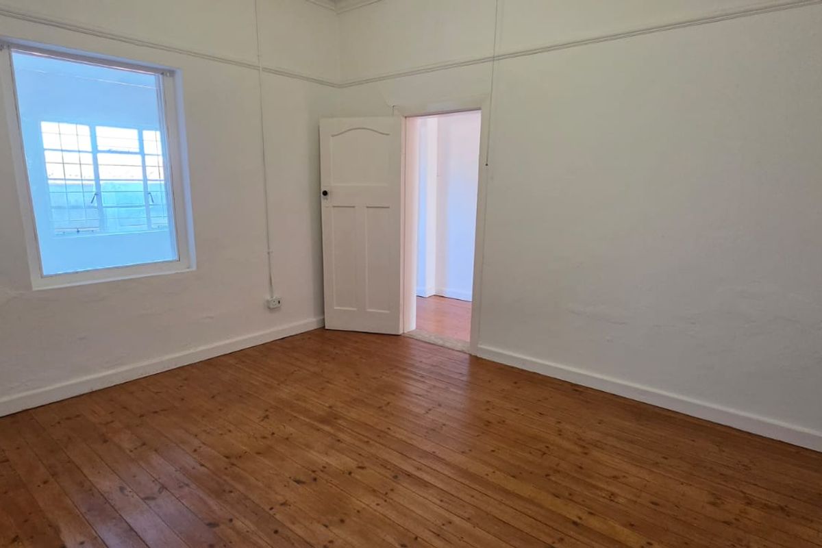An empty bedroom featuring original timber flooring, white walls with picture rails, and a casement window, offering a blank canvas for renovation.