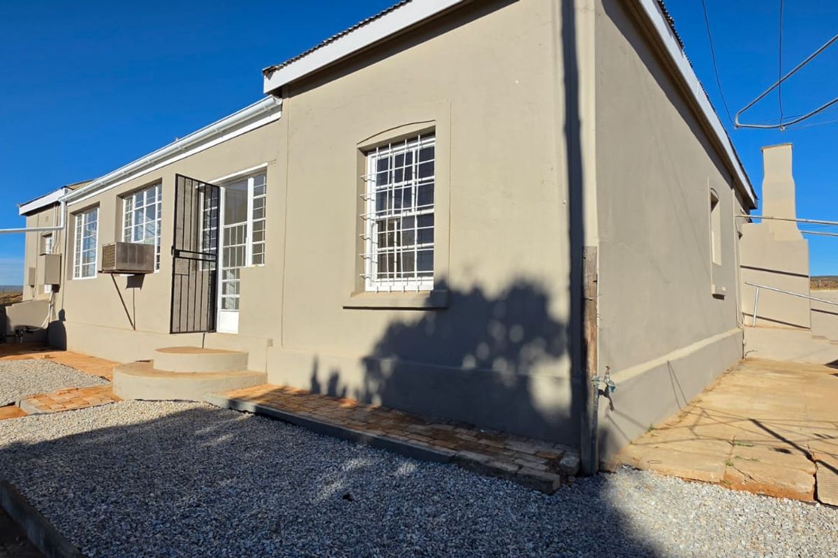 Rear exterior view of the house featuring a water storage tank, security bars on windows, and a paved outdoor area.