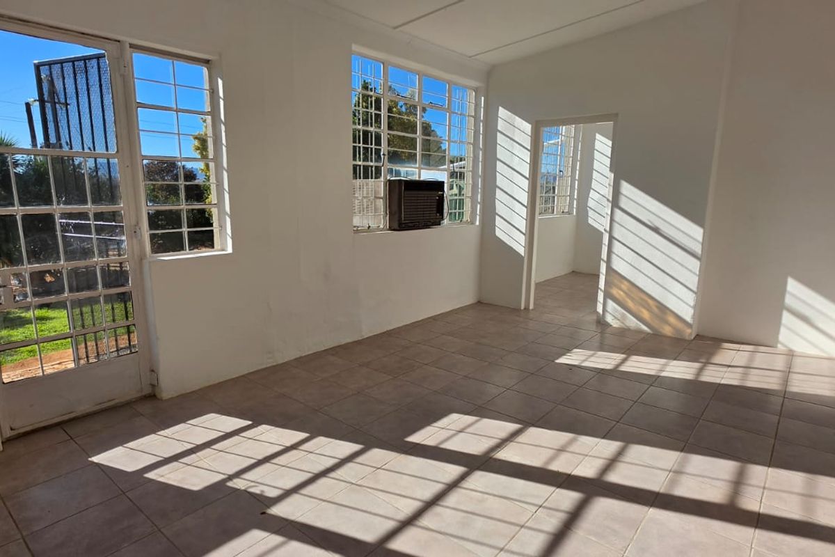 A bright, empty living area featuring tiled flooring, steel-framed windows, and a window-mounted air conditioning unit, offering a blank canvas for interior design.