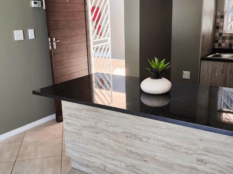 Modern kitchen featuring a granite breakfast bar, wood-look cabinetry, double sink, and tiled flooring, with direct access to an exterior security gate.