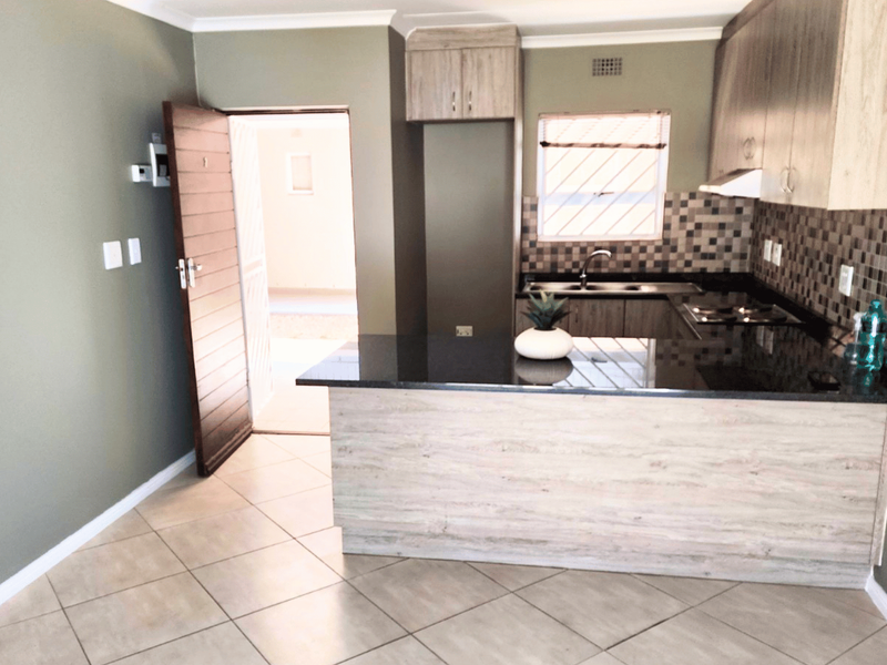 Open-plan kitchen featuring modern wood-finish cabinetry, granite countertops, mosaic backsplash, and tiled flooring, with direct access to an exterior area.