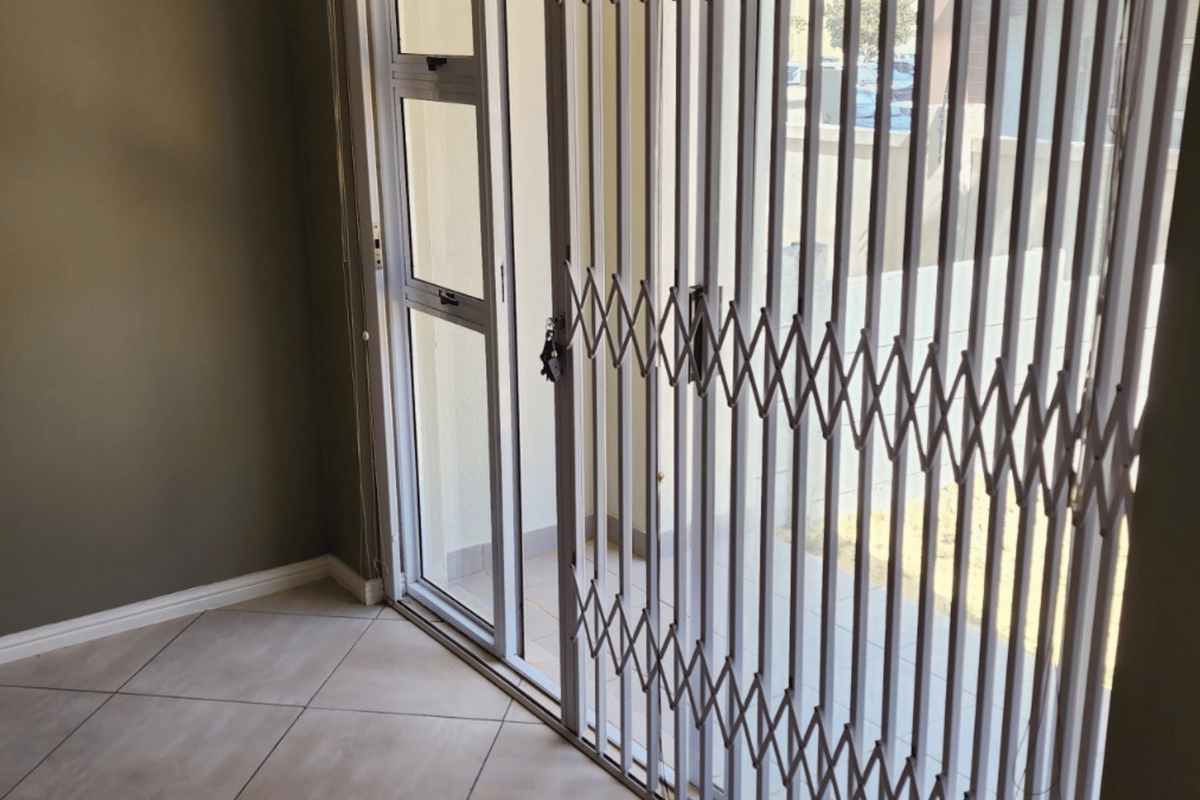 An empty living area featuring neutral tiled flooring, a sliding glass door, and a fitted security gate leading to an outdoor space.